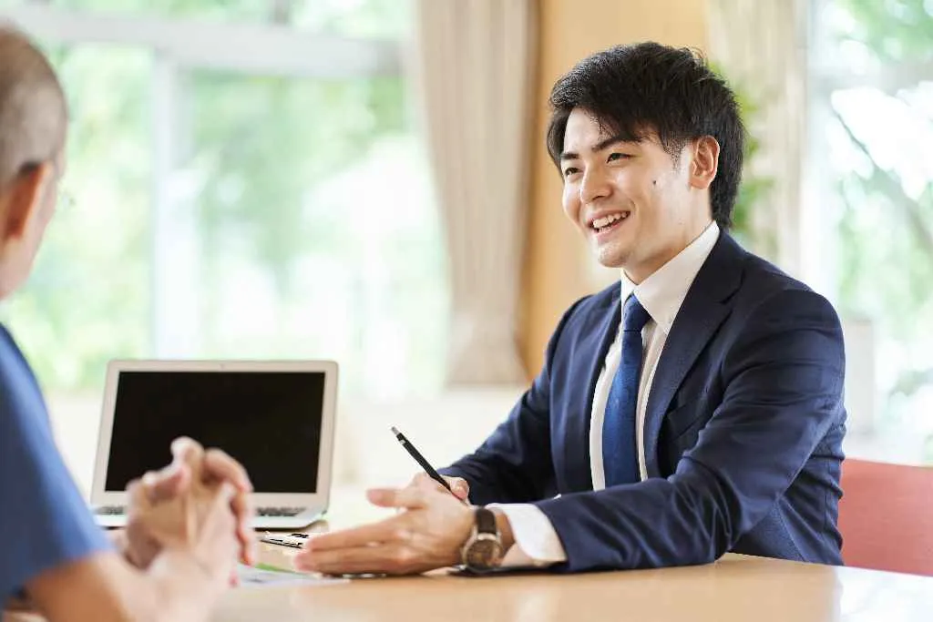 ノートパソコンに向かって笑顔を見せるスーツの男性